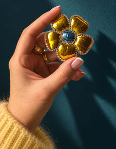 Broche fleur jaune et bleue tenue en main.