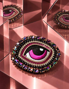 Broche Œil Céleste rose posée sur des surfaces miroir roses