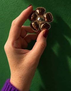 Broche fleur bronze et dorée tenue en main.